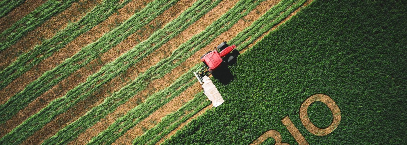 Bio concept and red tractor mowing green field.