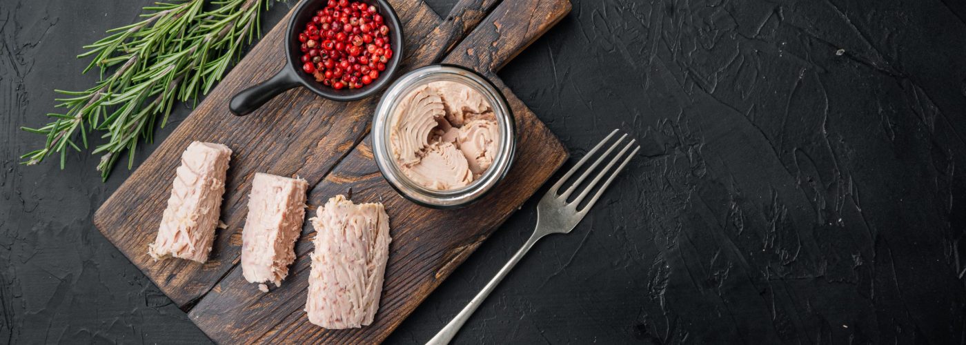 Canned tuna fillet meat in olive oil, on black background, flat lay  with copy space for text